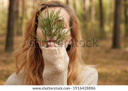 A Caucasian woman outdoors covering her face with a fir twig. The concept of unity with nature and wellness.