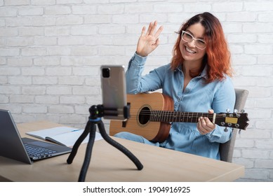 Caucasian woman playing guitar live on a smartphone. The girl leads a music video blog