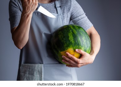 A caucasian woman is preparing to stab a watermelon using a sharp kitchen knife. A versatile image for summer fruits as well as a demonstration of force, metaphorical passive aggressive behavior