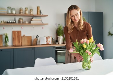 Caucasian woman putting fresh tulips into the vase - Shutterstock ID 2130201881