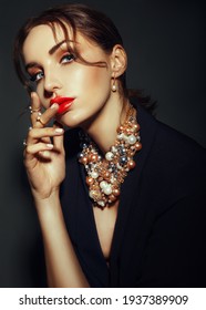 caucasian Woman with red lips in dark suit shows beads necklace and ring