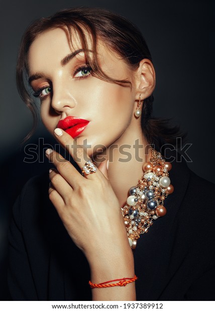 caucasian Woman with red lips in dark suit shows\
beads necklace and\
ring