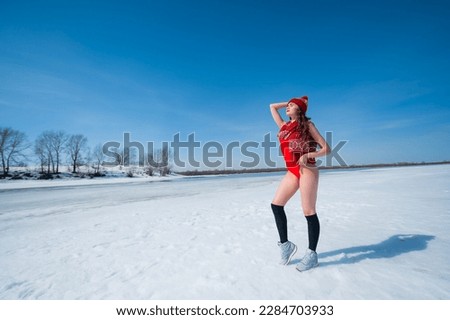 Caucasian woman in a red swimsuit resting on the shore of the frozen sea in winter. 