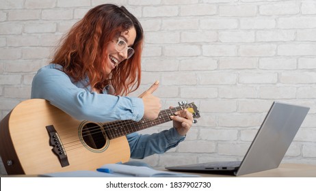 Caucasian woman remotely teaches guitar playing on laptop. Online music training