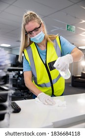 Caucasian Woman Sanitizing An Office Wearing Hi Vis Vest, Gloves, Safety Glasses And Face Mask, Using Disinfectant And Wiping Surfaces. Hygiene In Workplace During Coronavirus Covid 19 Pandemic.