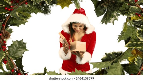 Caucasian woman in Santa costume opening gift, wearing a red hat. Sporting short black hair, enjoying surprise of her present - Powered by Shutterstock