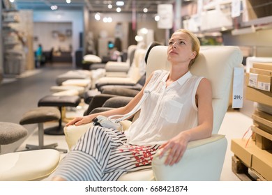 Caucasian Woman Shopping For Furniture, Recliner And Home Decor In Store. Lady Sitting On Reclining Chair Imagining Her New Home Architectural Arrangement.