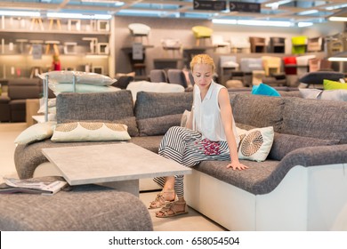 Caucasian Woman Shopping For Furniture, Sofa And Home Decor In Store. Lady Sitting On Couch Imagining Her New Home Architectural Arrangement.