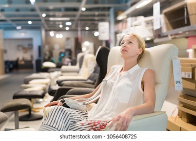 Caucasian Woman Shopping For Recliner And Home Decor In Furniture Store. Lady Sitting On Rocking Chair Imagining Her New Home Architectural Arrangement.