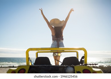 Caucasian woman sitting on beach buggy by the sea wearing straw hat looking toward sea with hands up. beach break on summer holiday road trip. - Powered by Shutterstock