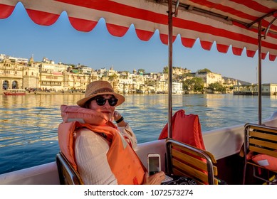 A Caucasian Woman Sitting On A Tour Boat Wearing A Lifejacket In Lake Pichola With Udaipur India In The Background