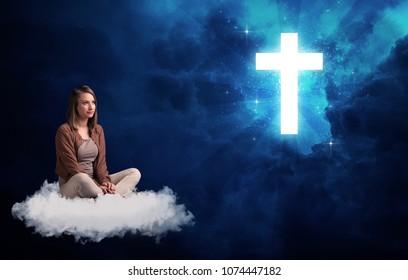 Caucasian woman sitting on a white fluffy cloud looking at a big, bright blue glowing cross