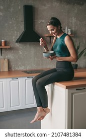 Caucasian Woman In Sportswear Resting At The Kitchen After Exercise And Eating A Bowl Of Porridge. Vegetarian Healthy Food.