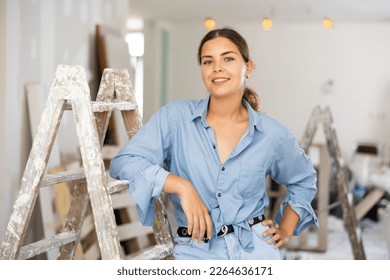 Caucasian woman standing in apartment during repair works, smiling and looking at camera.