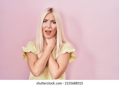 Caucasian woman standing over pink background shouting suffocate because painful strangle. health problem. asphyxiate and suicide concept. 
