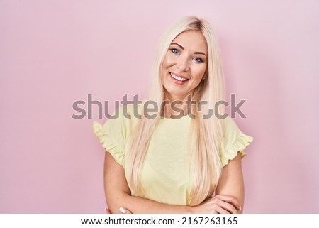 Caucasian woman standing over pink background happy face smiling with crossed arms looking at the camera. positive person. 