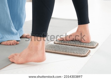 Caucasian woman stands on sadhu boards with therapist support.