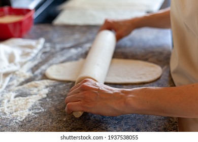 A caucasian woman is using an American rolling pin to roll over bread doughs to flatten and shape them. Authentic kitchen background homemade bread making concept. - Powered by Shutterstock