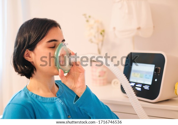 A caucasian woman using a\
cough assist ventilator mask for deep breaths, respiratory\
condition