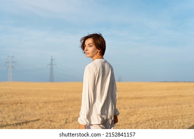 Caucasian woman walking wheat field dressed white clothes back view. Beautiful female brunet short hair standing agricultural field with blue sky background