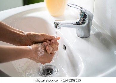 Caucasian woman washing her hands with liquid soap over a white sink in the bright natural sunlight as a preventive measure against coronavirus (Covid-19, SARS-CoV-2) infection. 