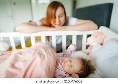 Caucasian woman watching her small baby child in the cradle bed happy mother taking care of her daughter at home in bright day with copy space - Shutterstock ID 2130476582