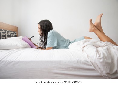 Caucasian Woman Wearing Only A T-shirt Writing In Her Notebook On The Bed With White Sheets