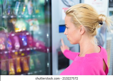 Caucasian woman wearing pink using a modern vending machine. Her right hand is placed on the key pad.
