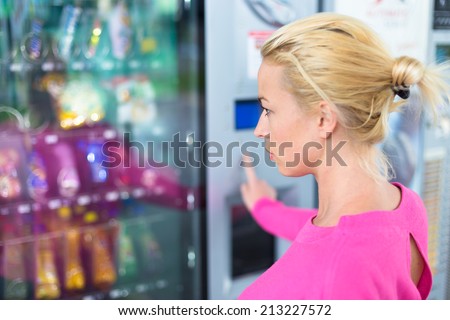 Caucasian woman wearing pink using a modern vending machine. Her right hand is placed on the key pad.