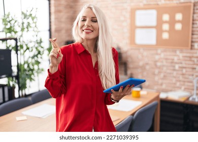 Caucasian woman working at the office with tablet gesturing finger crossed smiling with hope and eyes closed. luck and superstitious concept.  - Powered by Shutterstock