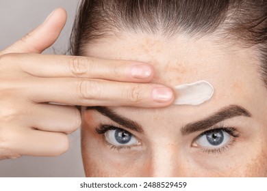 Caucasian woman's face with freckles or age spots, she smears creamon her forehead with her fingers, nice cream swatch, close up
