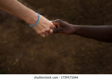 Caucasian woman's hand and African man's hand holding on to each other against a dark brown background with soft-focus edges - Shutterstock ID 1739571044