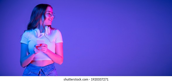 Caucasian woman's portrait on blue background in multicolored neon light. Beautiful model with headphones, phone. Concept of human emotions, facial expression, sales, ad, fashion. Copyspace. Flyer - Powered by Shutterstock