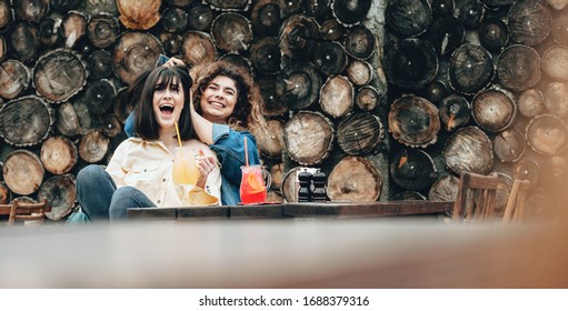 Caucasian women drinking cocktails outside on a wooden wall are playing together