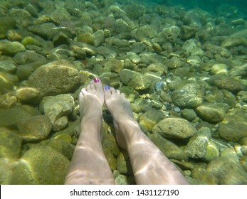 Caucasian Women With Purple And Pink Painted Toe Nails Relaxing With Her Feet Floating Under The Water In The Mediterranean Sea. Light Reflects Through The Water. Concept Holiday Background.