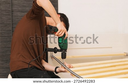A Caucasian worker assembles a slatted bed base with an electric drill.