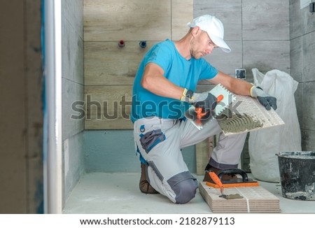 Caucasian Worker in His 40s Doing Remodeling in the Client’s Bathroom Installing Wooden Like Ceramic Tiles. Modern Design. Renovation Work Theme. Side View