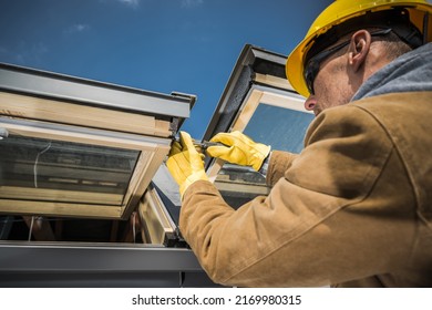 Caucasian Worker Wearing Safety Helmet And Protective Gloves Carrying Out Repair Works On Roof Skylight Windows Using His Screwdriver.