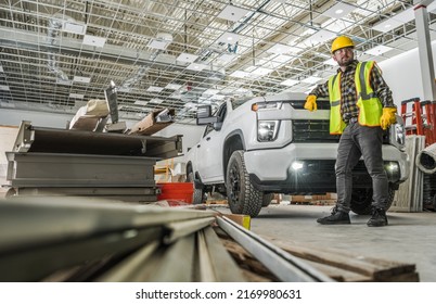 Caucasian Worker Wearing Yellow Hard Hat Inside Developed Warehouse Building Staying Next To His Modern Pickup Truck Commercial Vehicle. 