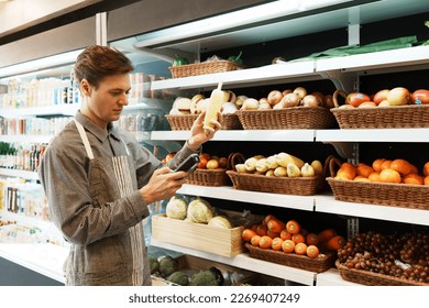 Caucasian young adult employee is filling out information about the quality and freshness of corn on the shelf with barcode scanner. Salesman is checking the stock of fruit in the basket on shelf. - Powered by Shutterstock