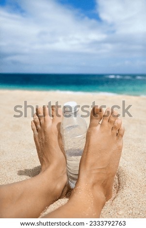 Caucasian young adult woman feet and water bottle on beach.