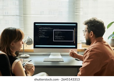 Caucasian young adult woman and Caucasian middle aged man collaborating at desk, analyzing neural network code displayed on computer monitor, discussing software development process - Powered by Shutterstock - Get 15% off with code: PIKWIZARD15