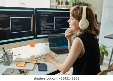 Caucasian young adult woman wearing headphones working on neural network development at computer workstation, smiling while coding on multiple monitors with programming interface visible