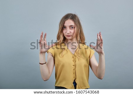 Caucasian young blonde woman showing space betweem palms wearing fashion yellow shirt isolated on gray background in studio. People sincere emotions, lifestyle concept.