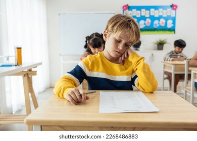 Caucasian young boy student doing an exam test at elementary school. Adorable children sitting indoors on table, feeling upset and depressed while writing notes, learning with teacher at kindergarten. - Powered by Shutterstock