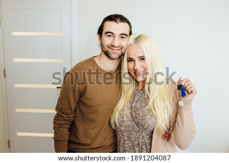 caucasian young couple showing keys and looking at camera, embracing, happy family celebrating relocation day, moving at new home, property owners,