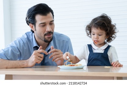 Caucasian Young Father With Beard Looking And Cheer Up Little Cute Daughter Trying To Eat Spaghetti With Spoon By Herself At Home And Adorable Kid Girl Enjoy Eating With Face Is Mess Up With Ketchup