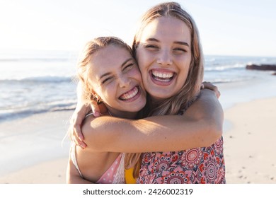 Caucasian young female friends embracing on a sunny beach. Their laughter and closeness capture a moment of joy and friendship outdoors.