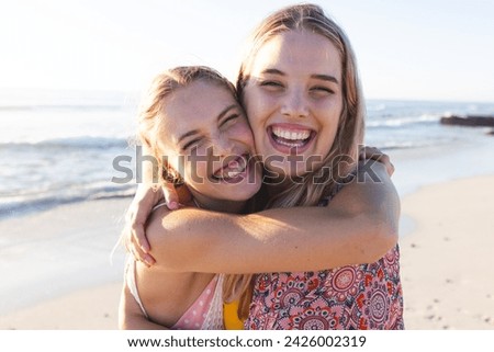 Caucasian young female friends embracing on a sunny beach. Their laughter and closeness capture a moment of joy and friendship outdoors.
