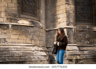 Caucasian young female stands by historic stone architecture with gothic window. - Powered by Shutterstock